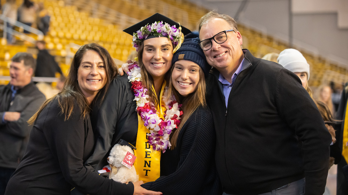 Family and their student pose at commencement in the Kibbie Dome.