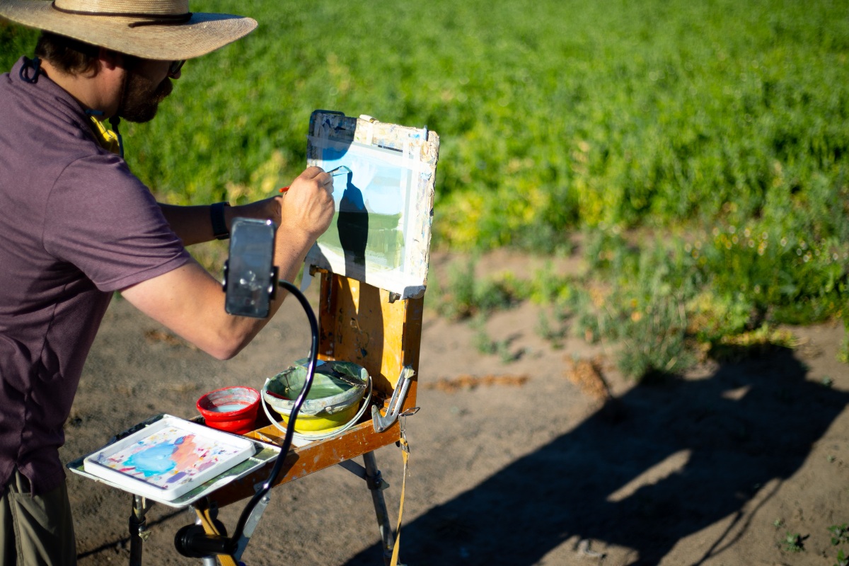 Art supplies and easel stand in a field overlooking a stream.