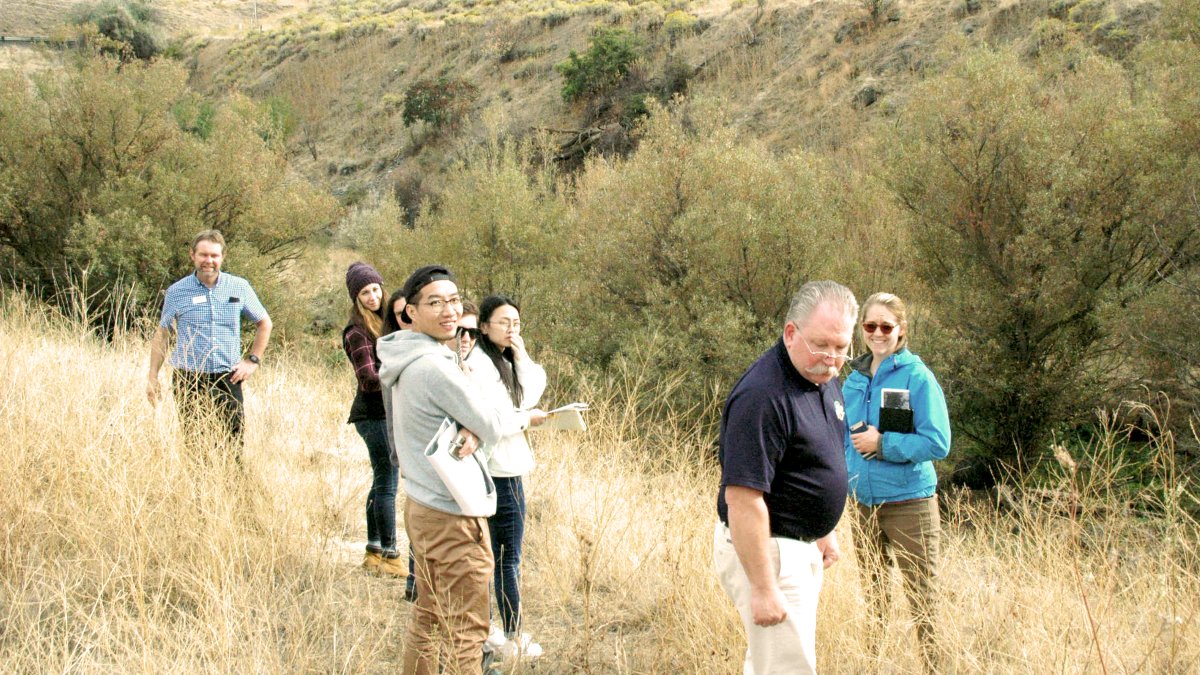 Students and faculty stand in a group in an area of wild grass with hills rising behind them.