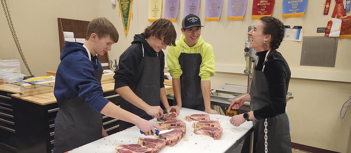 An instructor in a classroom and students with cuts of beef on a table.