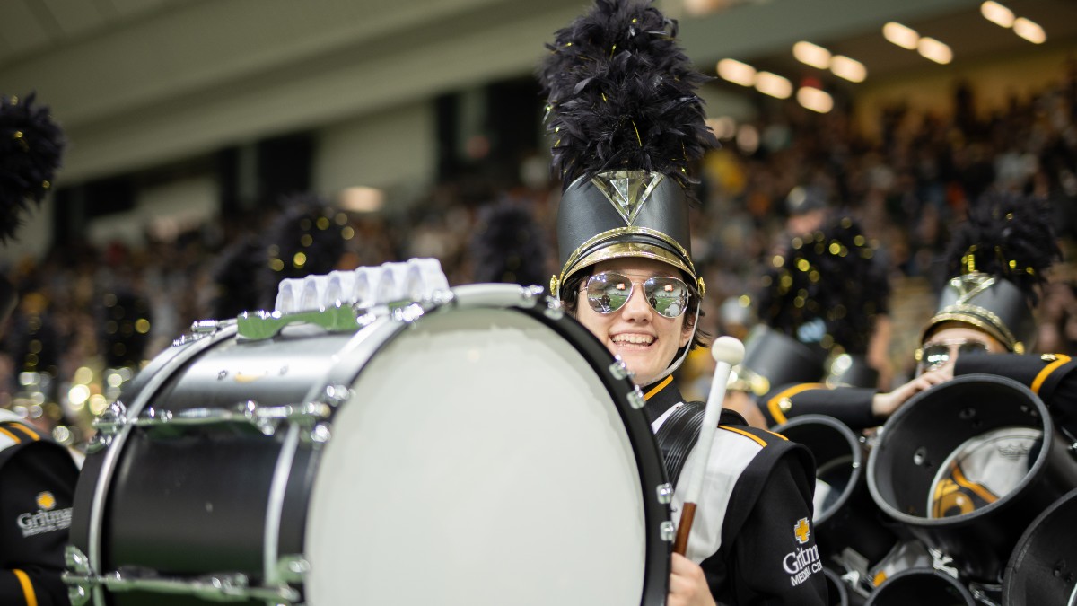 A female bass player smiles at the camera while she marches onto the Kibbie Dome field.