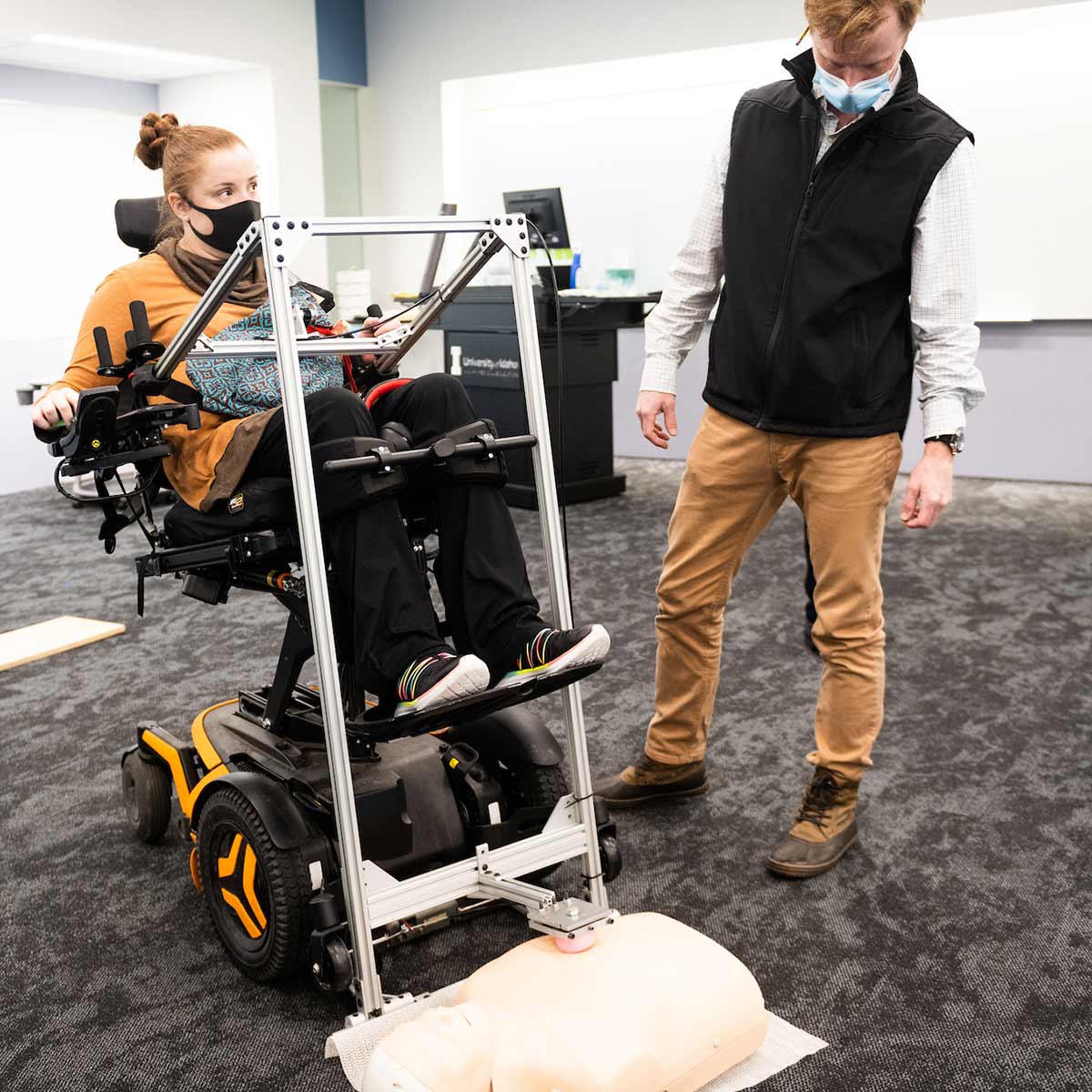 Engineering students help a student in a wheelchair use the assistive CPR device, which uses a lever-action to augments force and achieve necessary chest compression.