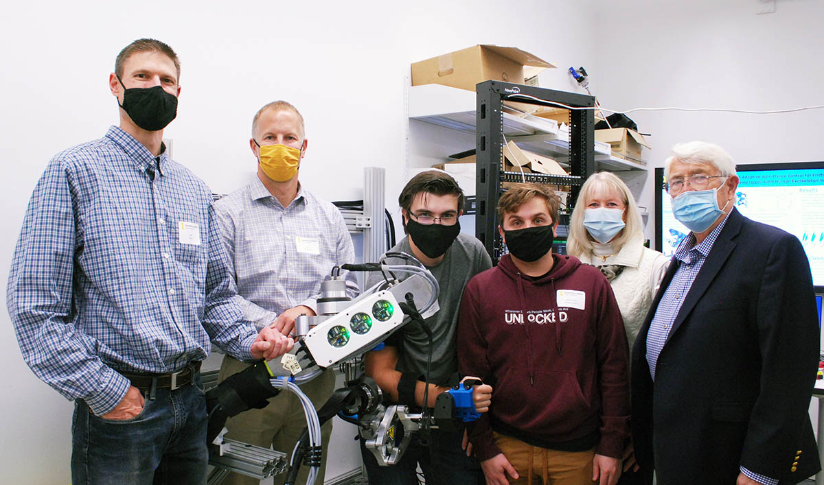 Students and faculty stand in front of a large robotic device to help stroke patients.