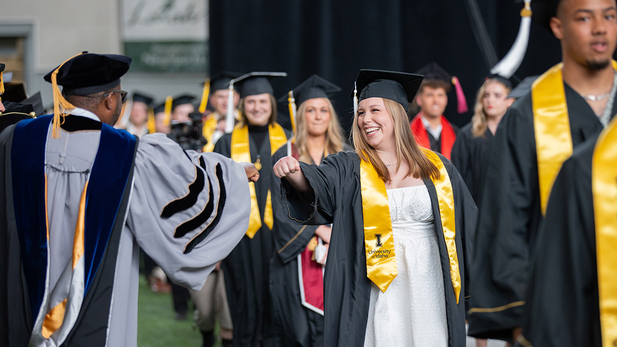 A professor fist bumping a student during graduation