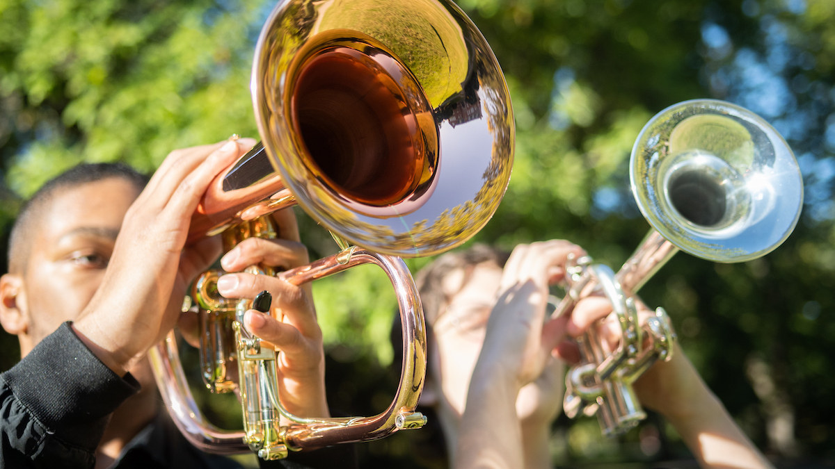 Two musicians play a silver and a gold trumpet outdoors