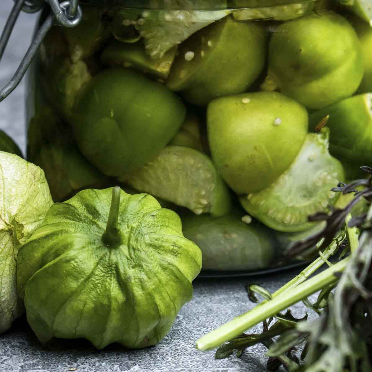 Tomatoes on table in front of bottled tomatillos.