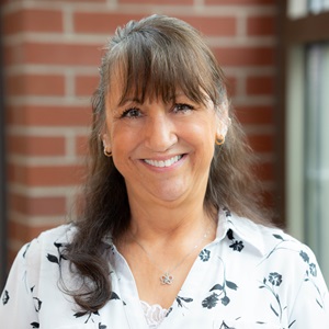 With hair pulled up in a half-ponytail, Renee smiles in a floral shirt at the camera.
