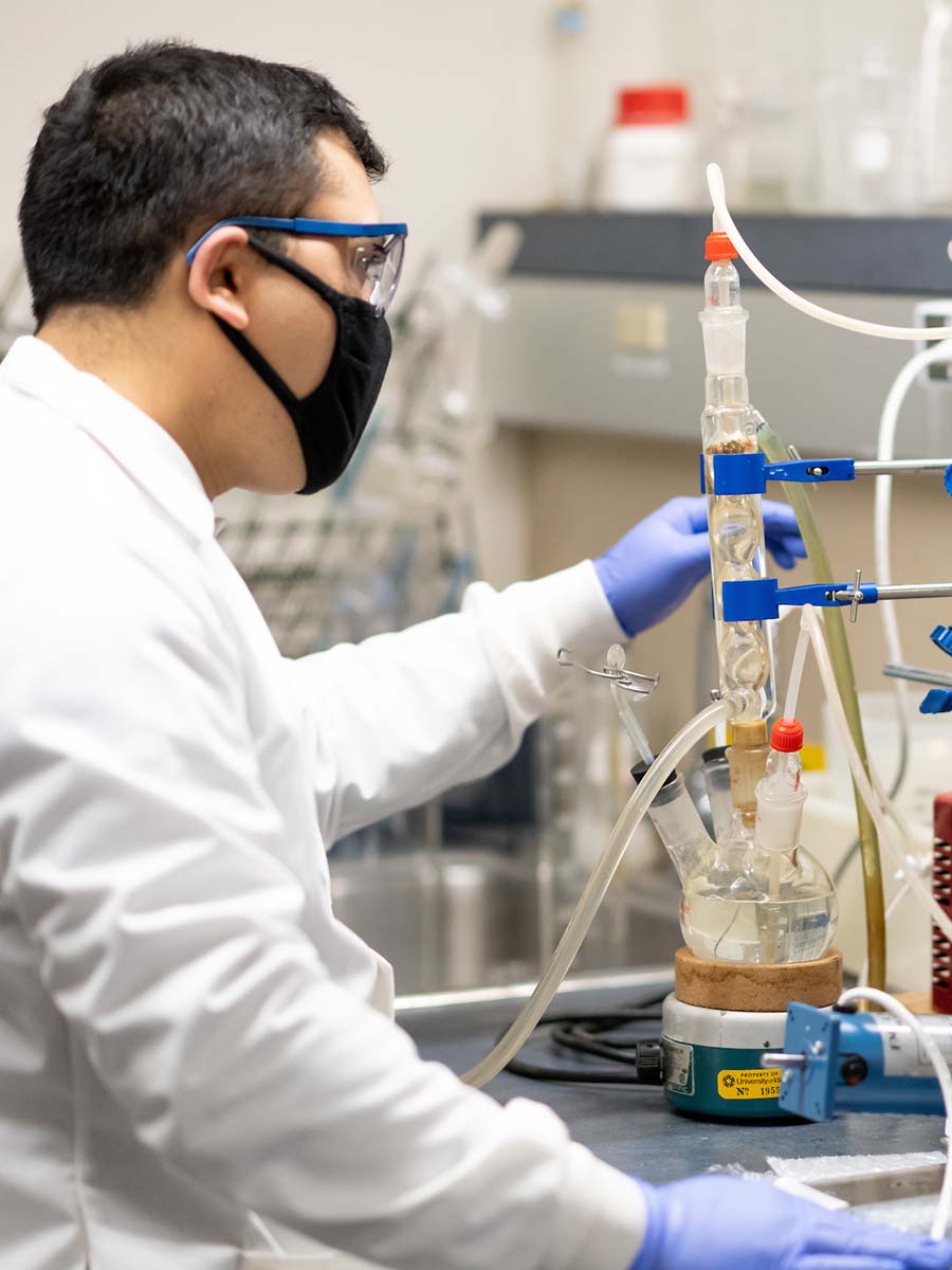 Bishal Thapa stands in a lab next to a plasma reactor, a device that breaks down air and water molecules using electricity. 