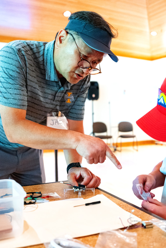 Man wearing visor pointing to student building a drone.