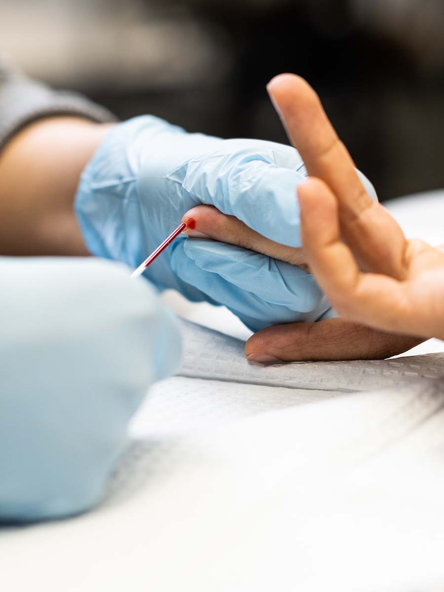 A pair of gloved hands draw blood from a finger.