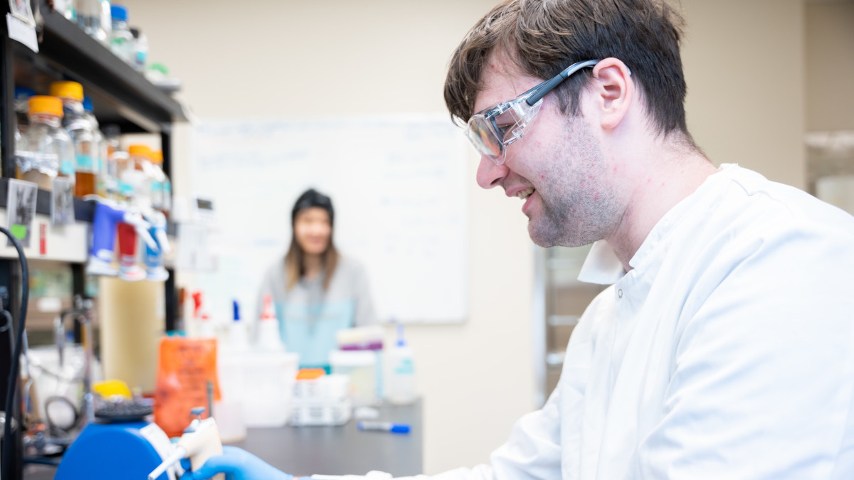 Smiling man wearing lab coat and safety glasses.