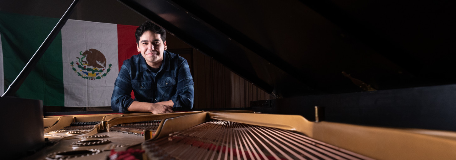 man standing behind a piano with the Mexican flag behind him.