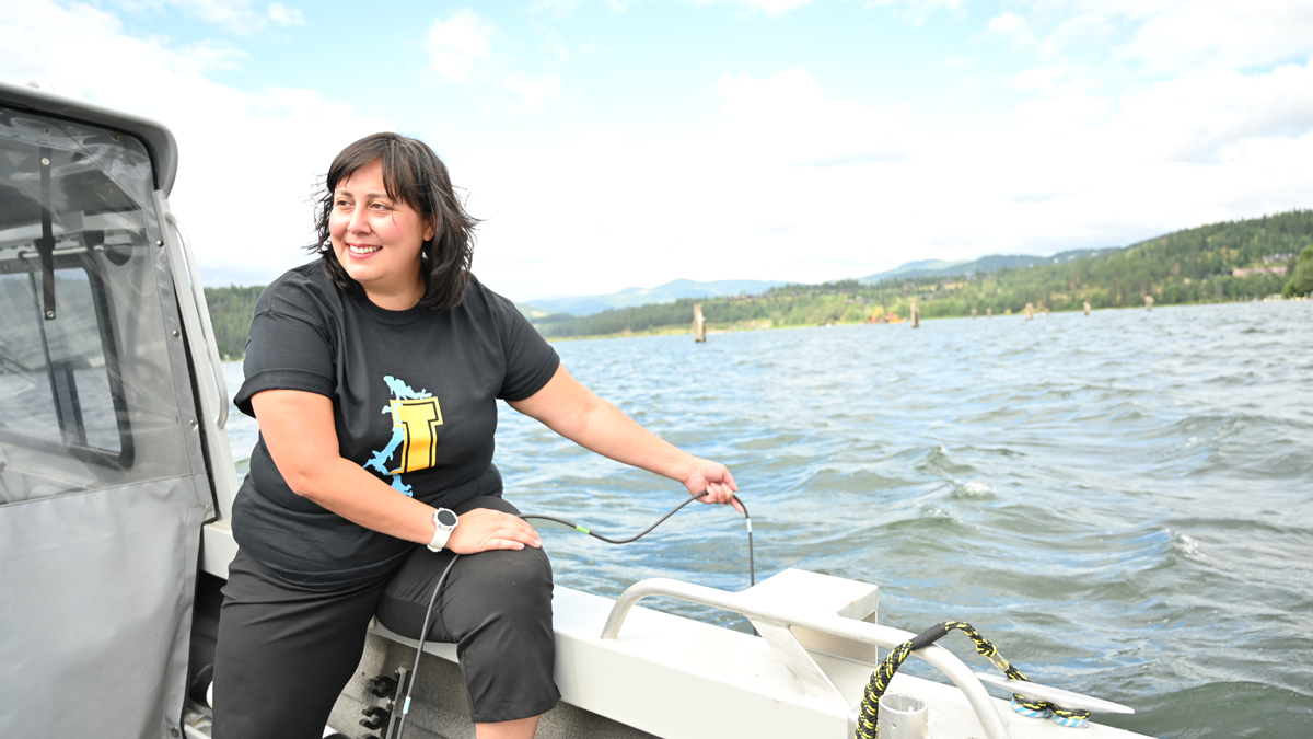 Krystal Saunoa stands in a boat and lowers a water sampler into Coeur d'Alene Lake