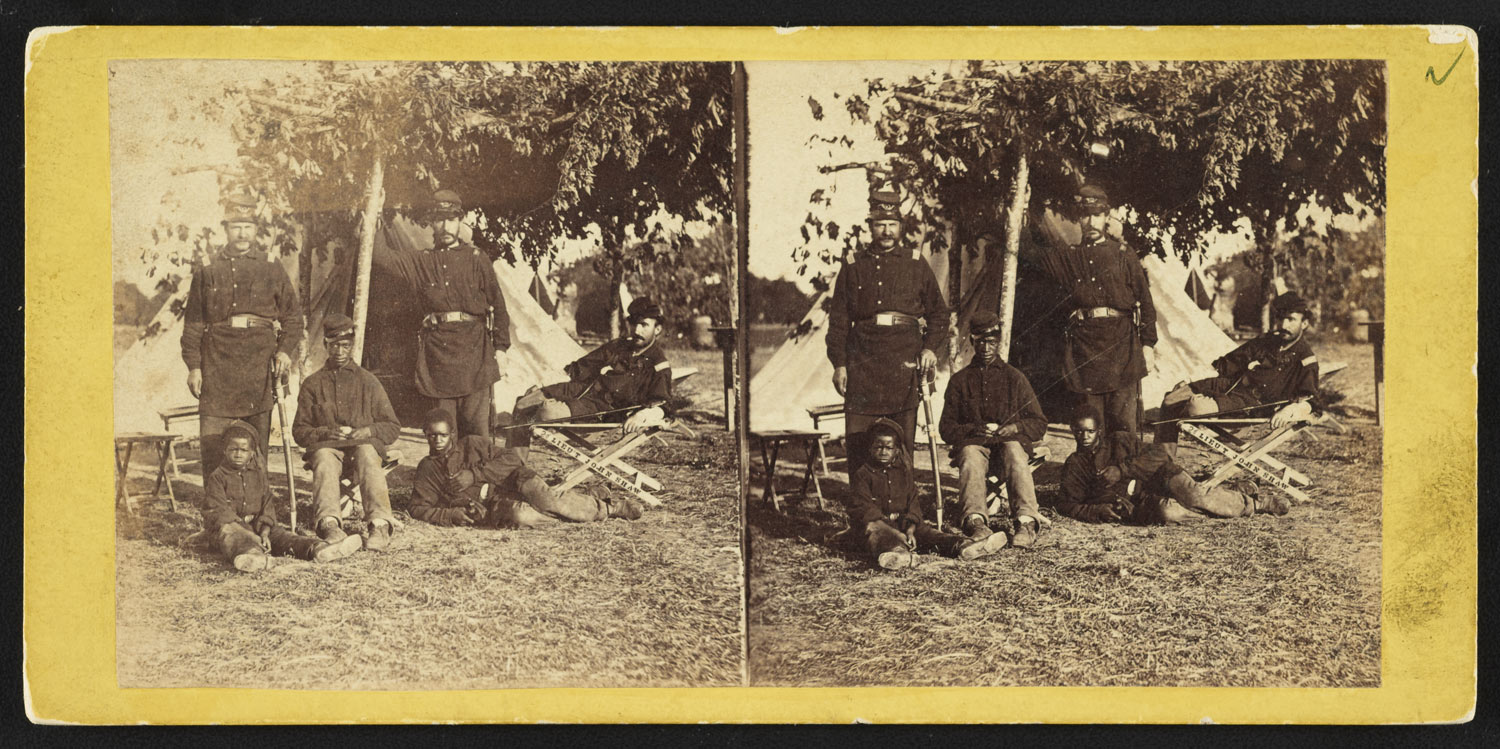 Stereograph showing Capt. B.S. Brown (left); Lt. John P. Shaw, Co. F 2nd Regt. Rhode Island Volunteer Infantry (center); and Lt. Fry (right) with African American men and boy at Camp Brightwood, D.C..
