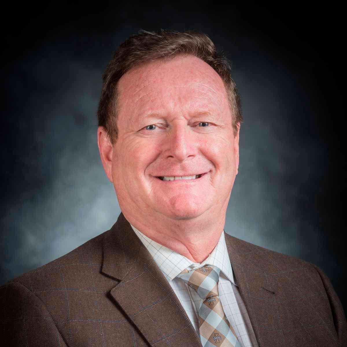 Brent Olmstead smiles in business attire.