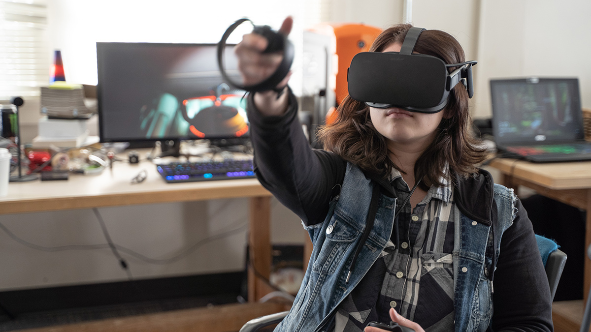 A woman wears a visor over her eyes and extends her hand, which holds a controller.